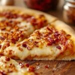 A slice of pizza topped with chili crunch, showcasing crispy garlic, chili flakes, and melted cheese.